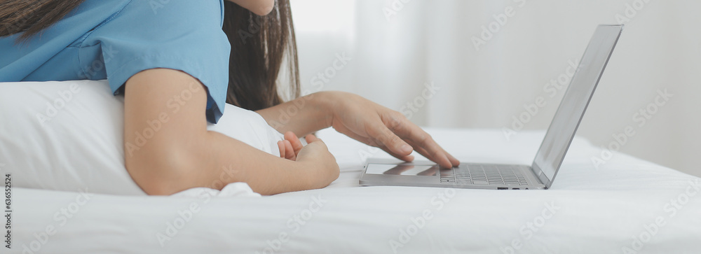 Naklejka premium Young Asian woman with beautiful face, long hair, blue shirt lying on bed in white bedroom at home with cup of coffee and video call with laptop talking to relatives on vacation. holiday concept.