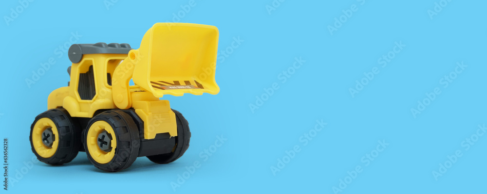 yellow plastic bulldozer toy isolated on blue background with copy space for toy store banner