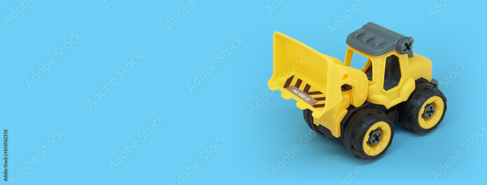 Naklejka premium yellow plastic bulldozer toy isolated on blue background with copy space for toy store banner