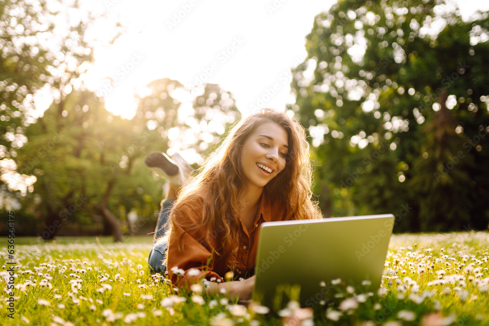 Cute young woman with laptop sits on the grass in the park outdoors. Online training, remote work. The concept of freelance, blog, business. Cute young woman with laptop sits on the grass in the park outdoors. Online training, remote work. The concept of freelance, blog, business.
