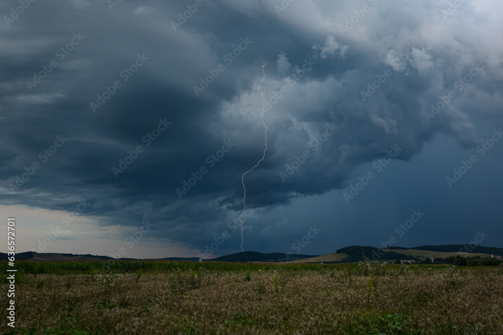 Dark thundercloud with narrow long vertical lightning bolt at dusk Dark thundercloud with narrow long vertical lightning bolt at dusk