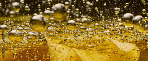 Deep fried potato chips under golden oil water. Frying rounded potatoes chip with hot boiling oil bubbles. Fast food and snack. Underwater cooking oily french fries or potatos chips in oils background