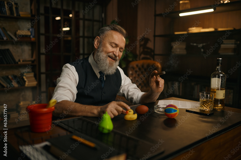 Funny elegant older businessman smoking cigar and playing toys at work table Funny elegant older businessman smoking cigar and playing toys at work table