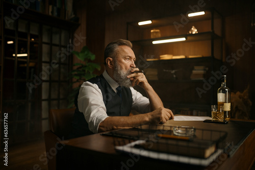 Pensive senior business man smoking cigar while sitting at work table