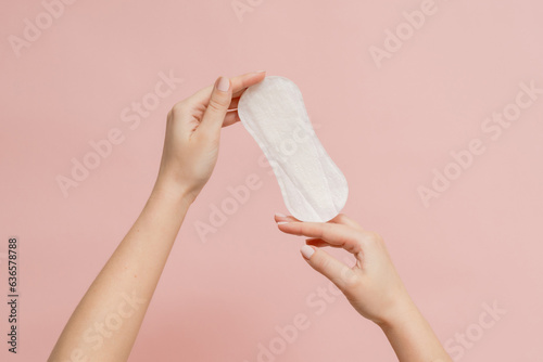 Sanitary napkin in woman's hand on pink background