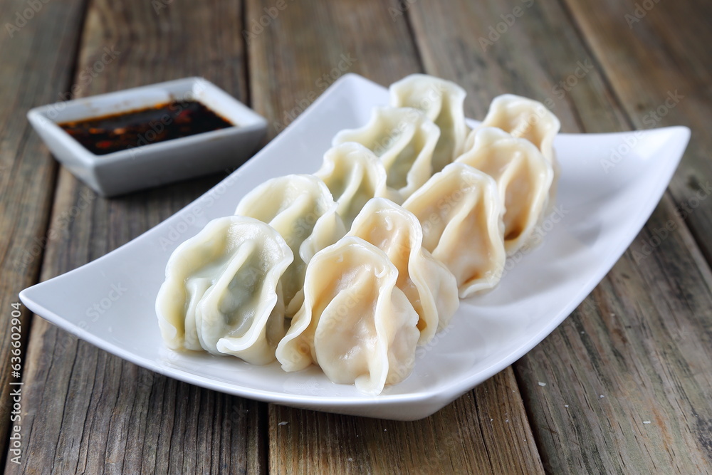 cabbage flavor and chives flavor dumplings on a white plate, with chili, garlic, ginger and soy sauce, wooden table, chop sticks cabbage flavor and chives flavor dumplings on a white plate, with chili, garlic, ginger and soy sauce, wooden table, chop sticks