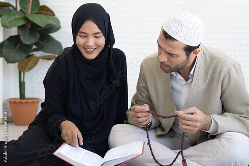 Islamic woman with hijab teaching Quran. Traditional muslim family couple reading Quran and praying together before iftar dinner during a ramadan feast at home.