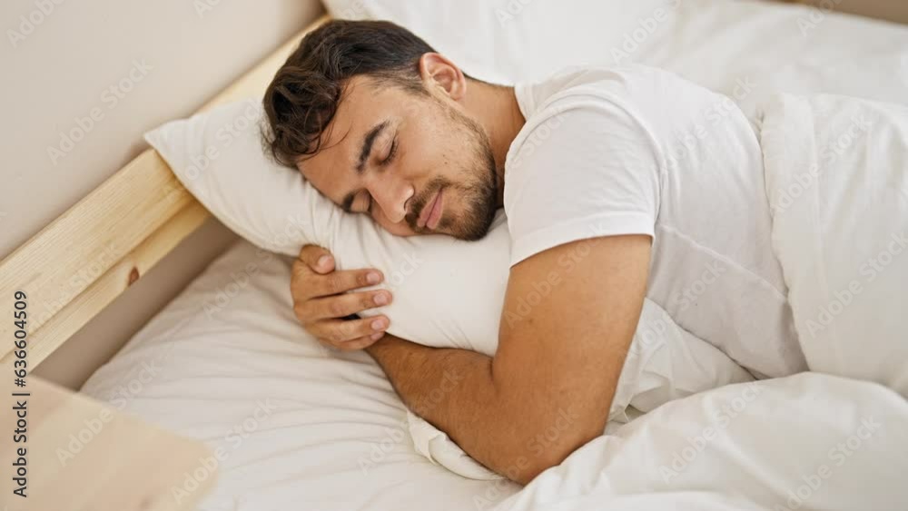 Young hispanic man hugging pillow lying on bed sleeping at bedroom