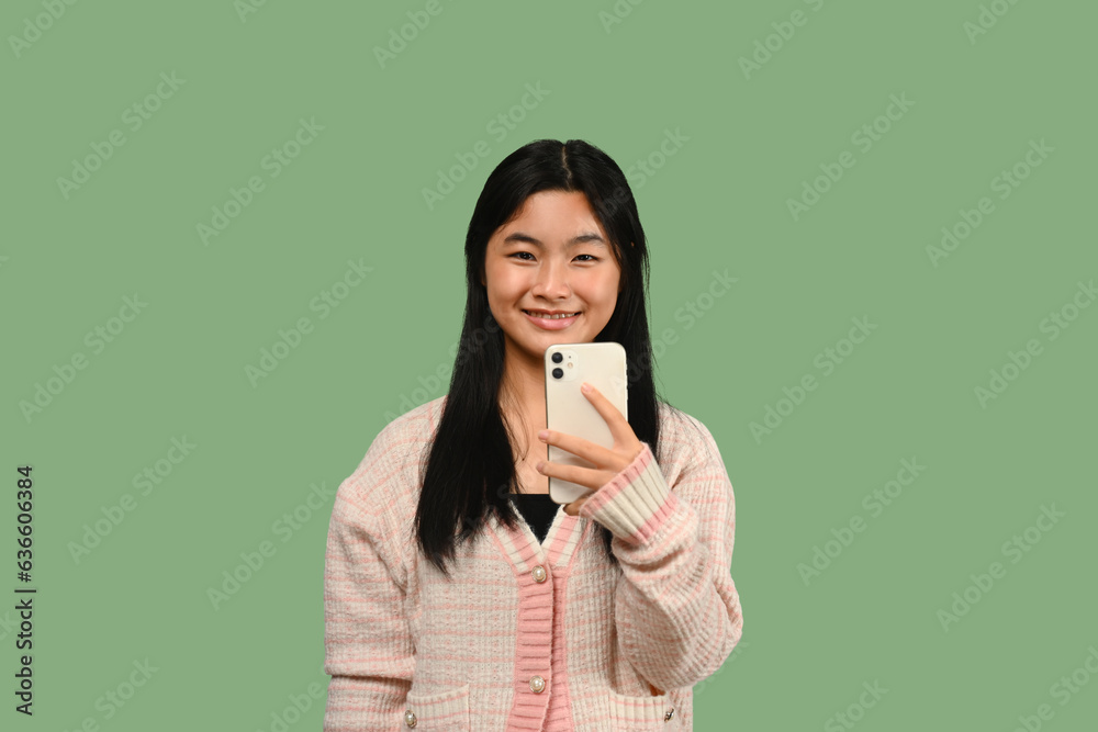 Happy teenage girl with smartphone standing on green background. People, technology and communication. Happy teenage girl with smartphone standing on green background. People, technology and communication.