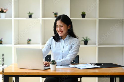 Charming female entrepreneur in blue shirt using laptop computer, doing online data market analysis at office