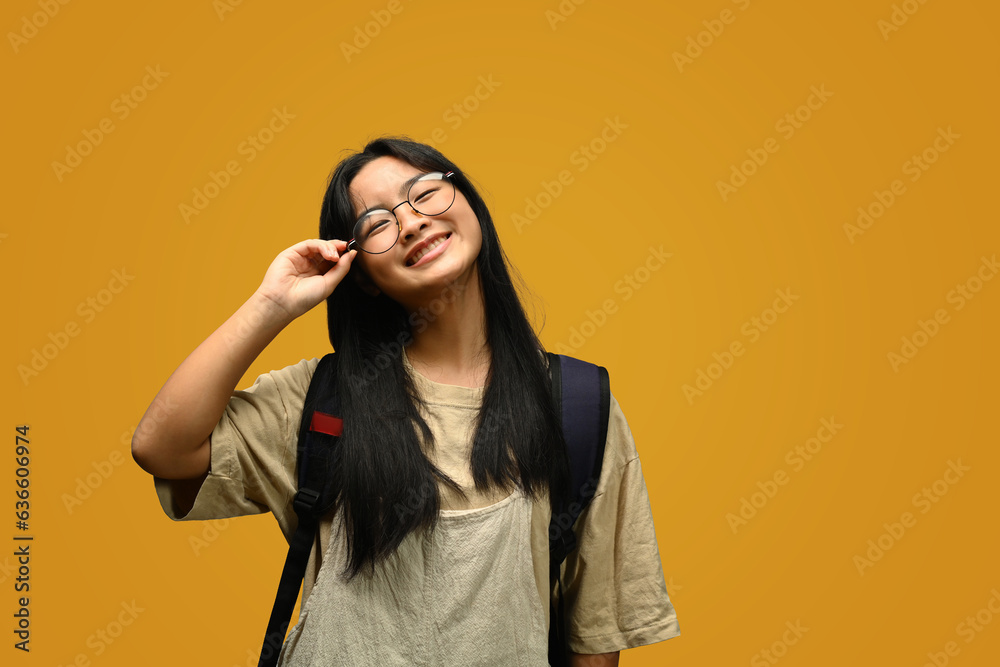 Smiling teenager schoolgirl wearing glasses with backpack standing on yellow background. Back to school concept Smiling teenager schoolgirl wearing glasses with backpack standing on yellow background. Back to school concept