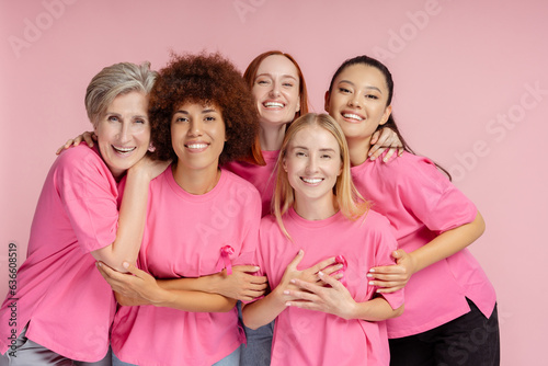 Group of smiling confident multiracial women wearing t shirts with pink ribbon looking at camera isolated on pink background Fototapeta
