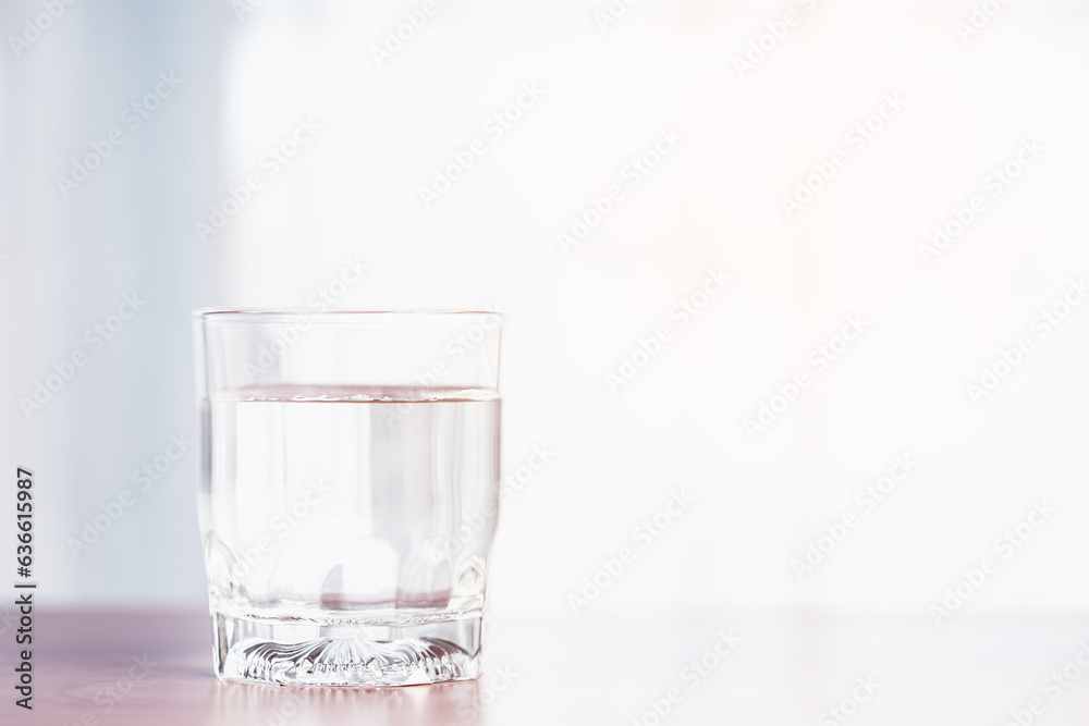 A clear glass containing water is placed upon a wooden table with soft orange sunlight from outside for the concept of healthy water consumption. A clear glass containing water is placed upon a wooden table with soft orange sunlight from outside for the concept of healthy water consumption.