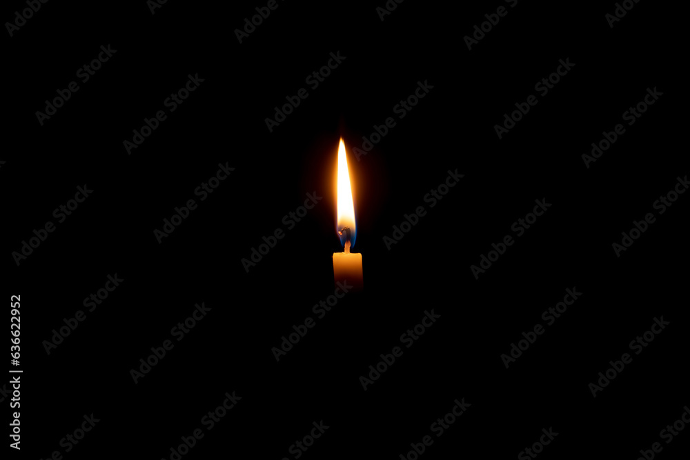 Single burning candle flame or light glowing on a small white candle on black or dark background on table in church for Christmas, funeral or memorial service with copy space. Single burning candle flame or light glowing on a small white candle on black or dark background on table in church for Christmas, funeral or memorial service with copy space.