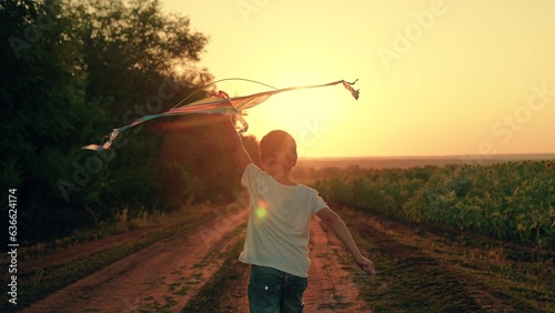 Fotografia Happy boy runs along country road, plays with toy kite, sunset