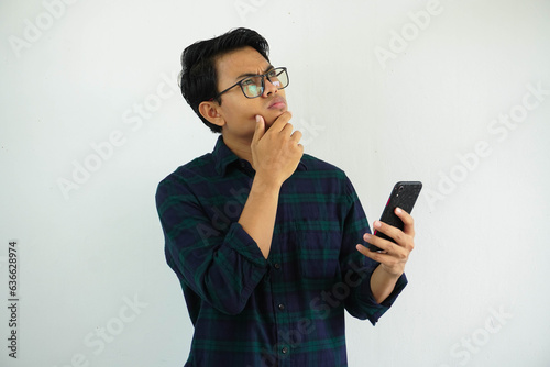 serious expression young asian man thinking something with while holding mobile phone isolated on white background.