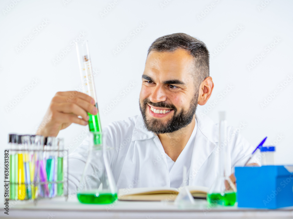 Young male scientist keenly observing a liquid sample held measuring cylinder while in a laboratory Young male scientist keenly observing a liquid sample held measuring cylinder while in a laboratory