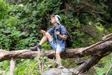 Young man traveler sitting on a fallen tree and looking at the compass in hand.