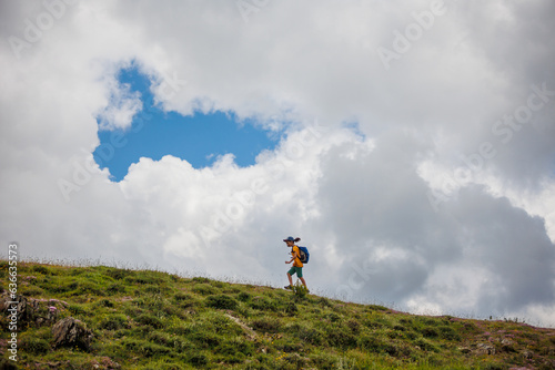 boy goes with a backpack against the backdrop of clouds in the mountains. child traveler with backpack  hiking  lifestyle concept