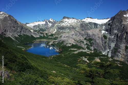 Small mountain lake surrounded by green forest and gray lifeless rocks under blue sky, Jakob lagoon in Nahuel Huapi National Park, Mountain landscape nature of Patagonia, Argentina