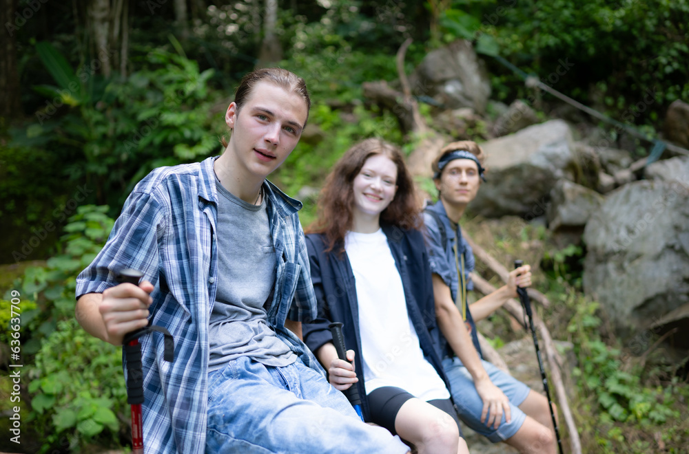 Group of friends with backpacks and sticks sitting on a fallen tree, Take a break during the hike Group of friends with backpacks and sticks sitting on a fallen tree, Take a break during the hike