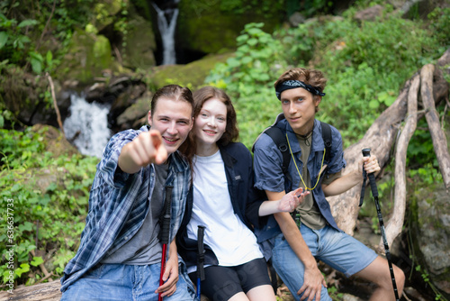 Group of friends with backpacks and sticks sitting on a fallen tree, Take a break during the hike