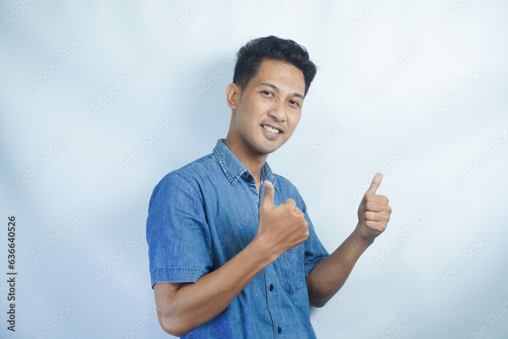 Young handsome Asian man wearing a blue shirt over isolated white background with thumbs up because something good has happened Young handsome Asian man wearing a blue shirt over isolated white background with thumbs up because something good has happened