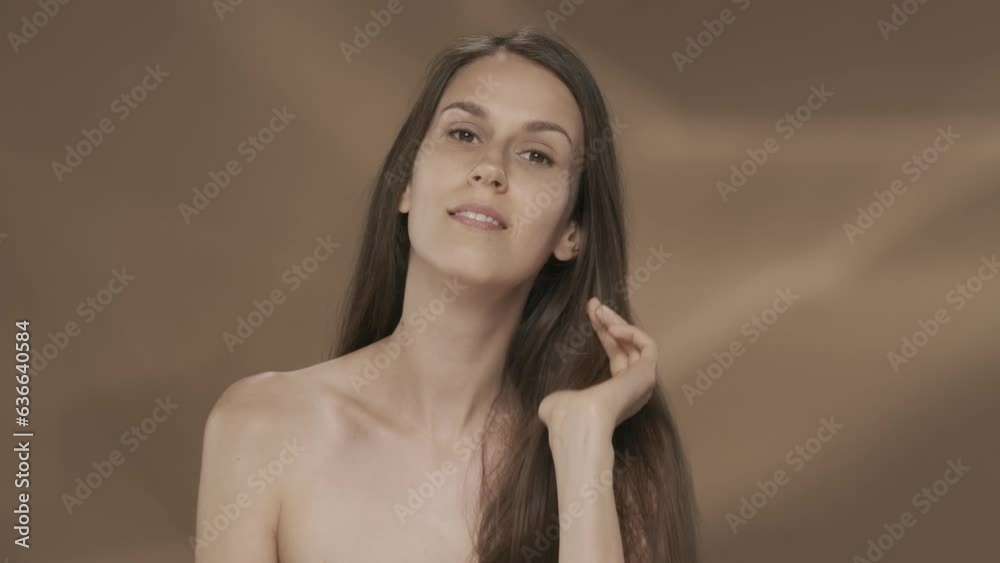 A woman demonstrates long silky, healthy and shiny hair. Seminude young woman in the studio on a brown background. Keratin straightening. Slow motion. HDR BT2020 HLG Material. A woman demonstrates long silky, healthy and shiny hair. Seminude young woman in the studio on a brown background. Keratin straightening. Slow motion. HDR BT2020 HLG Material.