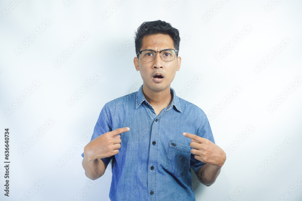 Image of amazed indignant surprised young man, being speechless, points at herself, wears blue shirt, asks why me, isolated over white background, stares concerned. Image of amazed indignant surprised young man, being speechless, points at herself, wears blue shirt, asks why me, isolated over white background, stares concerned.