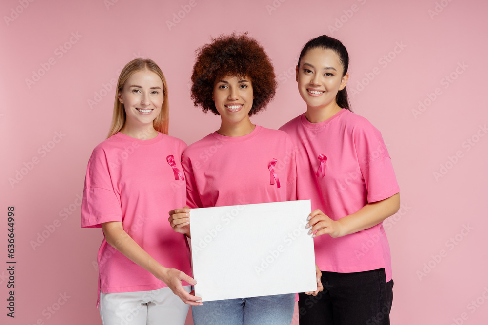 Beautiful smiling women with breast cancer pink ribbon holding empty board for text isolated on pink background, mockup. Breast cancer awareness month concept 