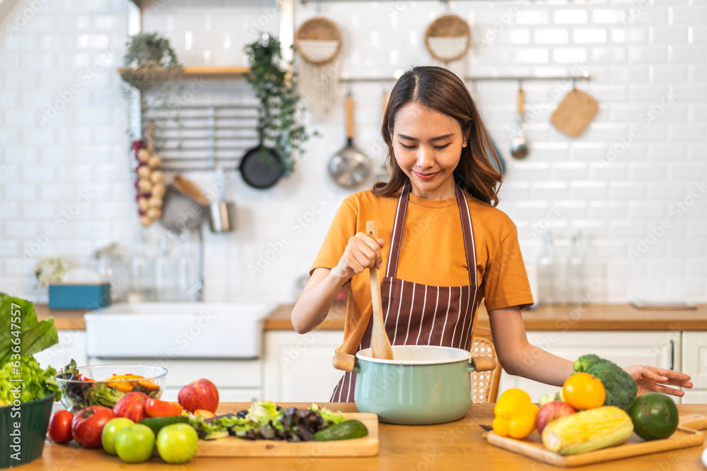 Young woman standing near stove and cooking, housewife, meal, chef, food.Happy woman looking and smelling tasting fresh delicious from soup in a pot with steam at white interior kitchen