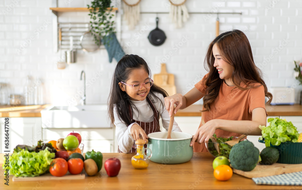 Portrait of enjoy happy love asian family mother with little asian girl daughter child help cooking food healthy eat with fresh vegetable testing smell soup in a pot with spoon.help mommy in kitchen