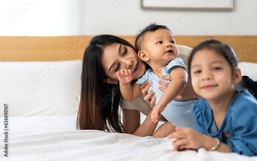 Portrait of enjoy happy love family asian mother playing with adorable little asian baby and sister girl, newborn, infant.Mom touching care with cute son in a white bedroom.Love of family concept