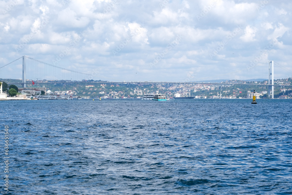 Wide angle landscape of Bosphorus Bridge and İstanbul with cloudy sky and wavy sea.