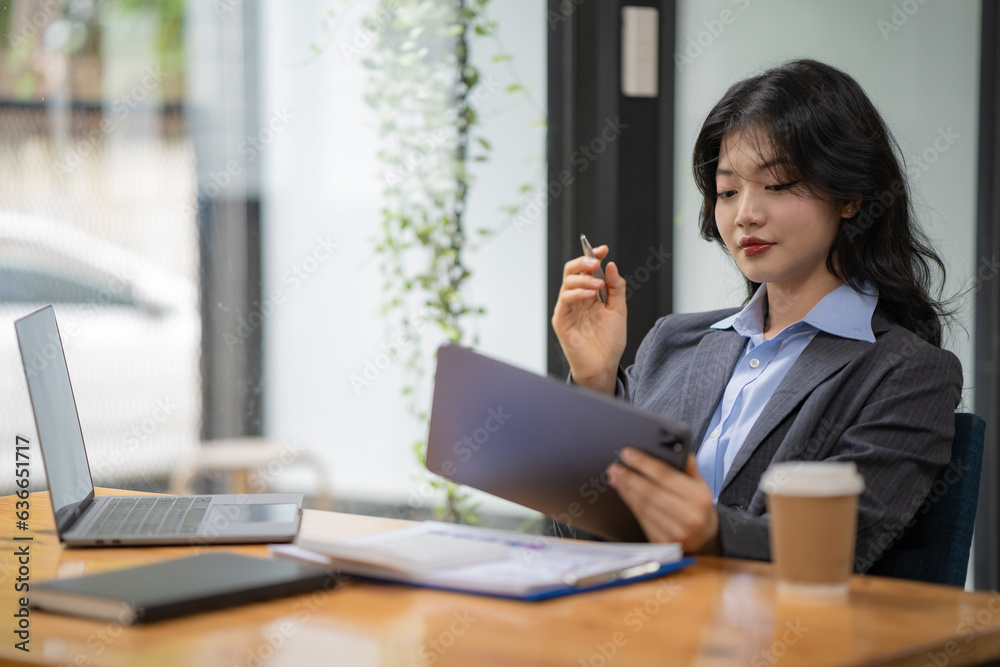 Attractive business Asian woman using a digital tablet while sitting at a workplace desk in an office. Attractive business Asian woman using a digital tablet while sitting at a workplace desk in an office.