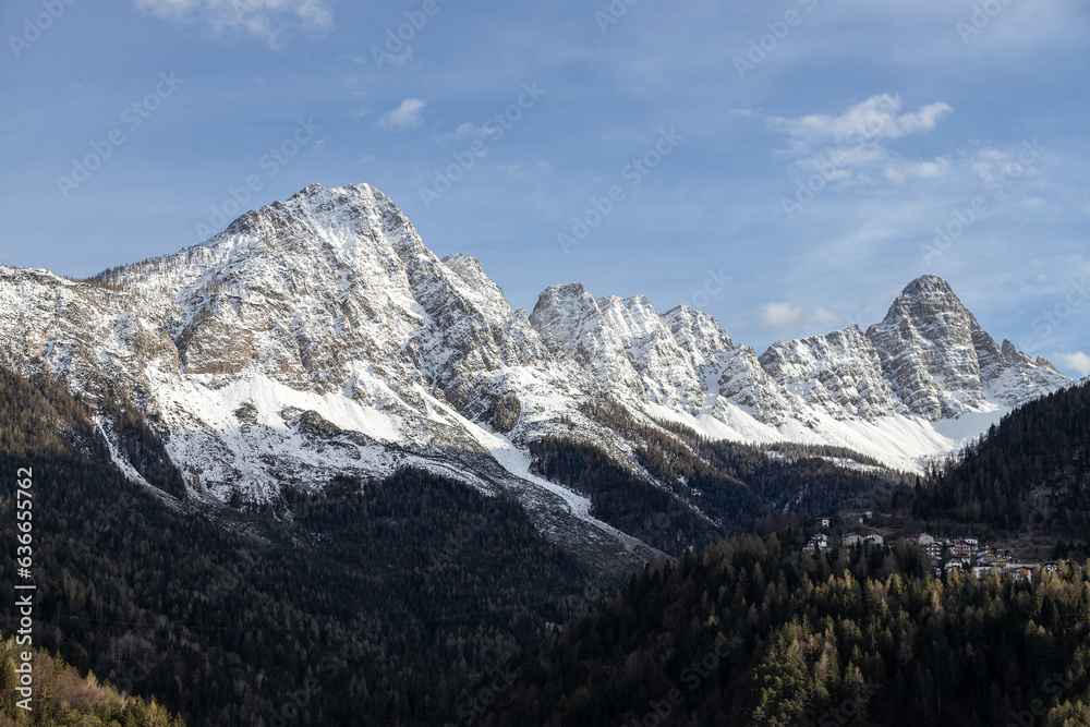 View of Cibiana di Cadore town at the foot of the snow peaked mountains. Blue sky with clouds in a sunny winter day; Dolomites, Italian alps, Italy View of Cibiana di Cadore town at the foot of the snow peaked mountains. Blue sky with clouds in a sunny winter day; Dolomites, Italian alps, Italy