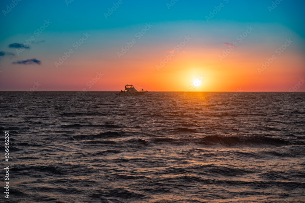 Beautiful nature scene of colorful sunset over ocean with boat on horizon