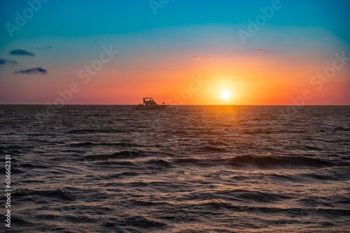 Beautiful nature scene of colorful sunset over ocean with boat on horizon