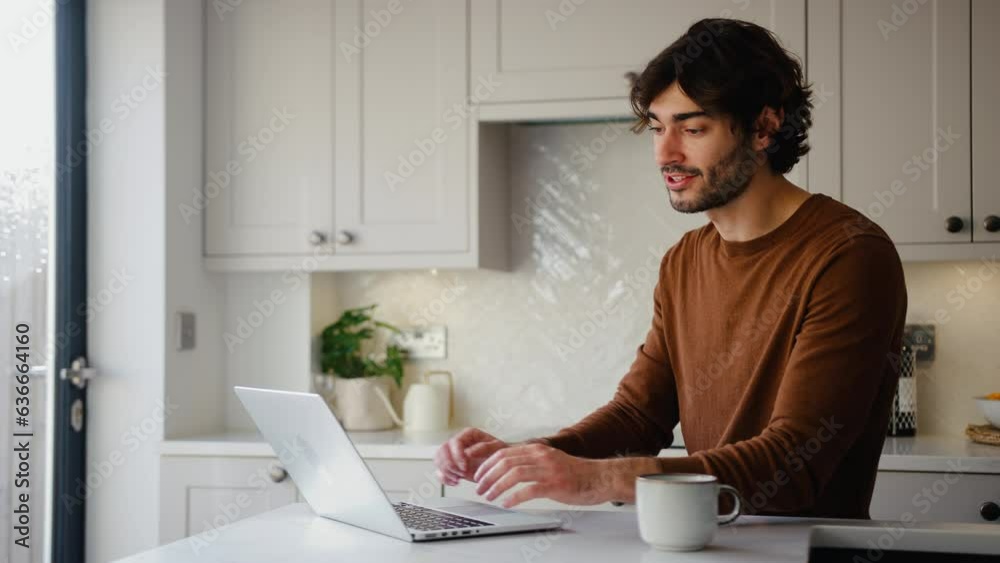Young man working from home on laptop sitting at kitchen counter - shot in slow motion Young man working from home on laptop sitting at kitchen counter - shot in slow motion