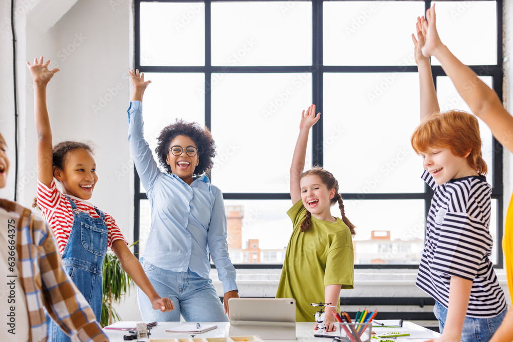 © JenkoAtaman - Group of schoolchildren and teacher standing together, celebrate successful completion of collective school work and raising their hand in class © JenkoAtaman - Group of schoolchildren and teacher standing together, celebrate successful completion of collective school work and raising their hand in class