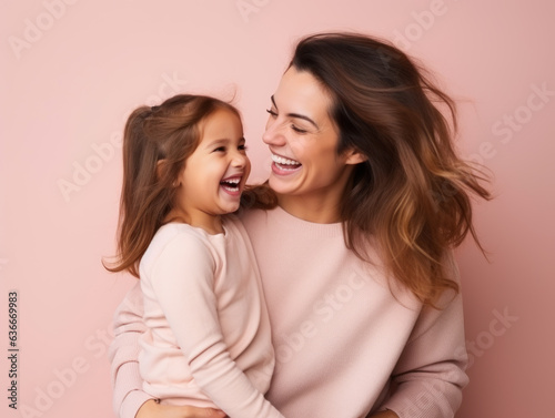 Photo of mother holding her little daughter in a good mood wearing a pink t-shirt on pink background