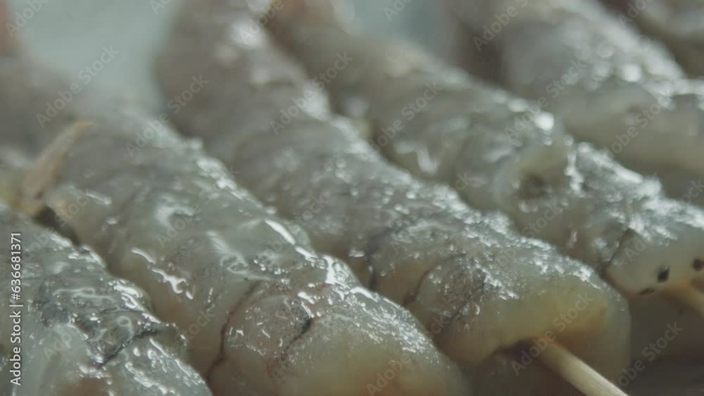 Spraying water on the raw peeled shrimps. Drops of water fall on the peeled raw shrimps, planted on sticks. Macro shot. Spraying water on the raw peeled shrimps. Drops of water fall on the peeled raw shrimps, planted on sticks. Macro shot.