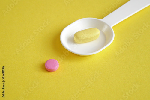 spoon with pills and tablets on yellow  background. checking ingredients and effectiveness of medicine photo