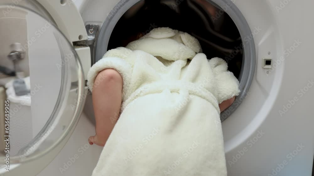 adorable cute baby boy in bathrobe putting or remove clothes from washing machine.kid playing with glass door.funny face emotions,top side view,preschooler child.4k bathroom interior.