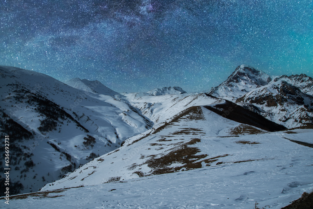 Beautiful night landscape, snow covered mountains in the night. Bright milky way galaxy behind them.