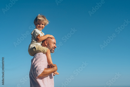 dad carries his son on his shoulders against the sky photo