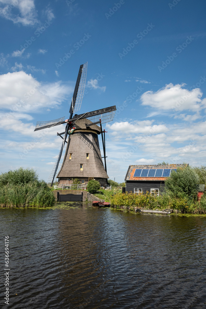 iconic smock ground sailer windmill in Kinderdijk Netherlands. Landmark buildings originally made to pump water out of low land polder to preserve land reclaimed from the sea. Solar sun panels on shed iconic smock ground sailer windmill in Kinderdijk Netherlands. Landmark buildings originally made to pump water out of low land polder to preserve land reclaimed from the sea. Solar sun panels on shed