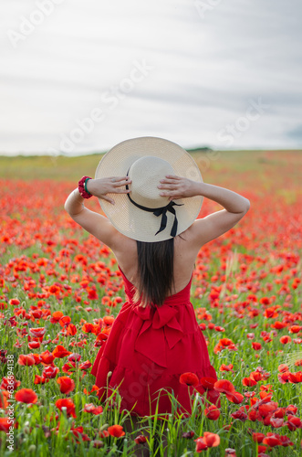 Ragazza pensierosa che indossa un cappello di paglia e passeggia in un campo di papaveri durante una bella giornata primaverile di fine maggio