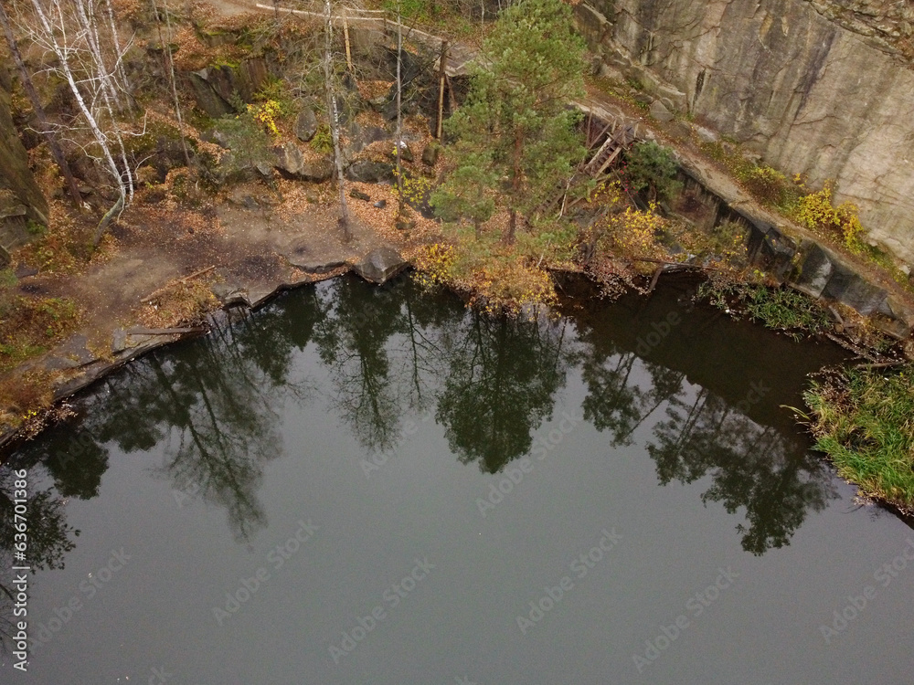 Picturesque aerial view of landscape with emerald lake and rocks in the middle of a coniferous autumn forest in Korostyshiv granite quarry, Zhytomyr district, northern Ukraine. Zhytomyr canyon Picturesque aerial view of landscape with emerald lake and rocks in the middle of a coniferous autumn forest in Korostyshiv granite quarry, Zhytomyr district, northern Ukraine. Zhytomyr canyon