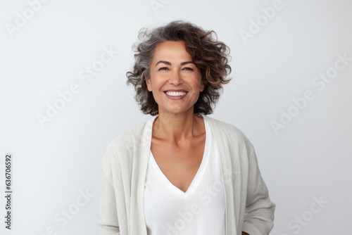 Medium shot portrait of a Brazilian woman in her 50s in a white background wearing a chic cardigan